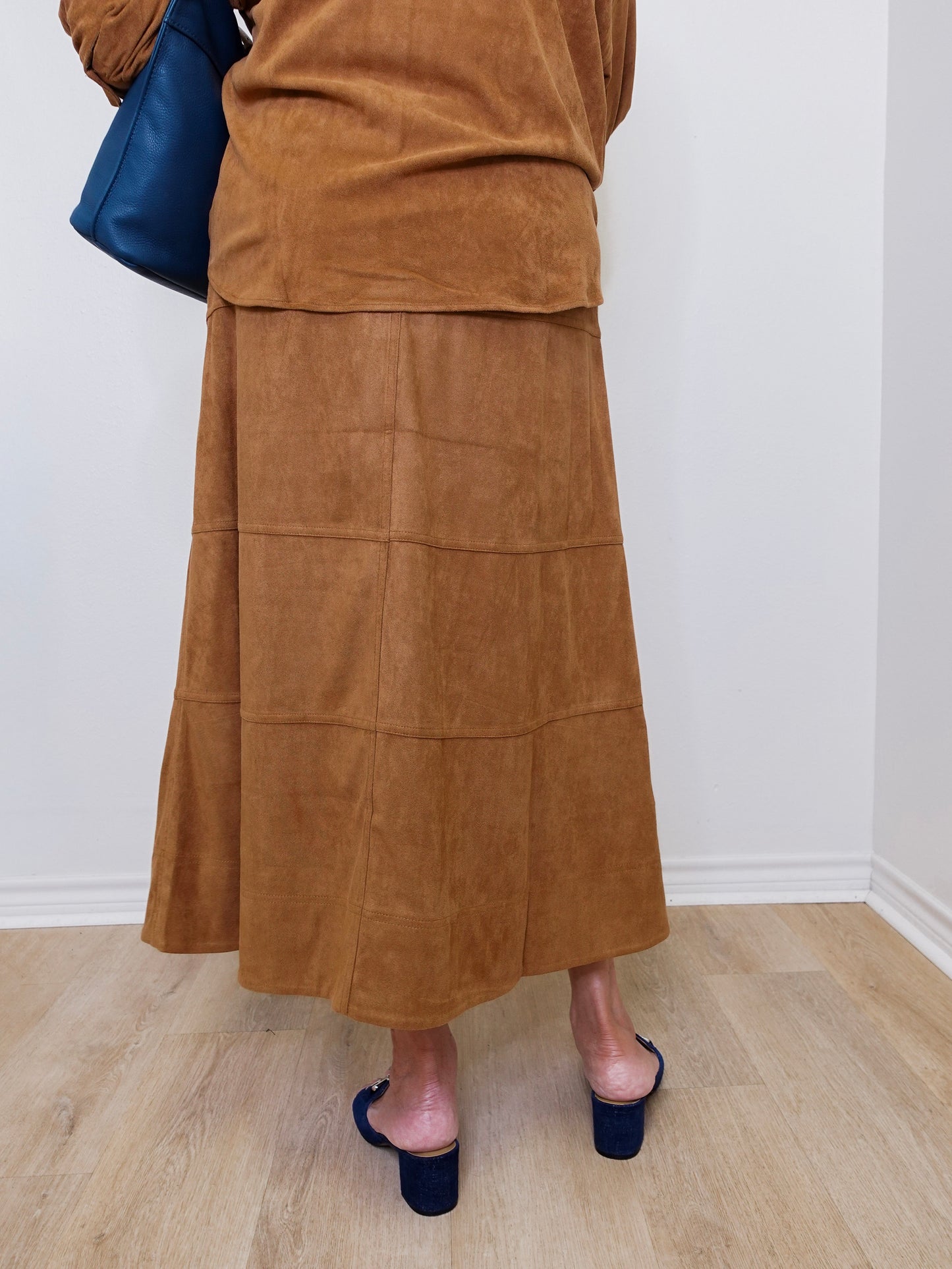Person wearing a brown suede skirt and navy shoes on a light wooden floor.