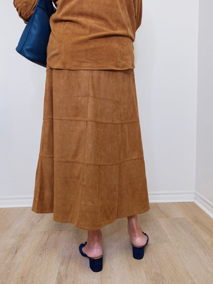 Person wearing a brown suede skirt and navy shoes on a light wooden floor.