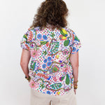 Person wearing a colorful floral shirt and beige shorts on a white background