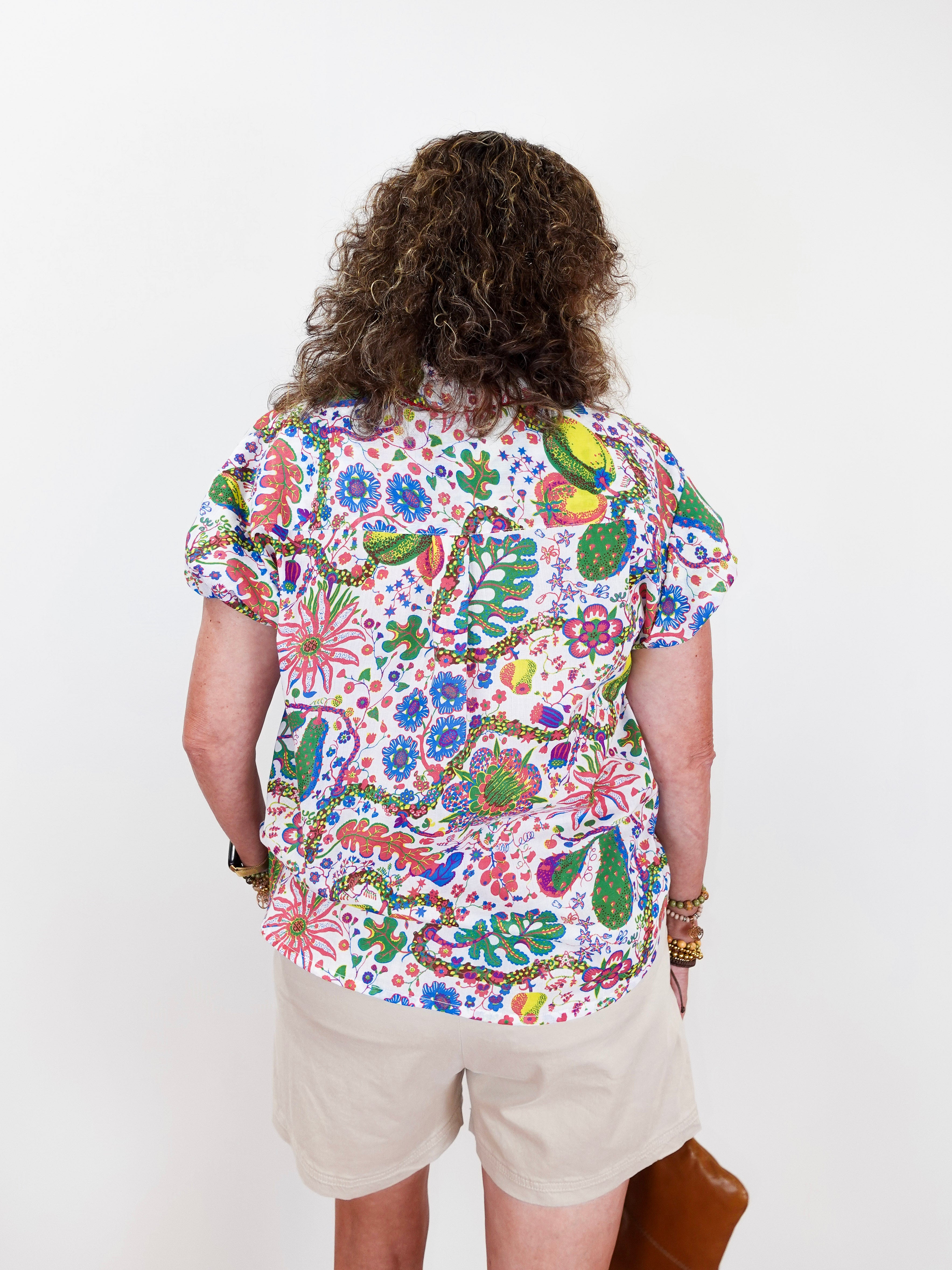 Person wearing a colorful floral shirt and beige shorts on a white background