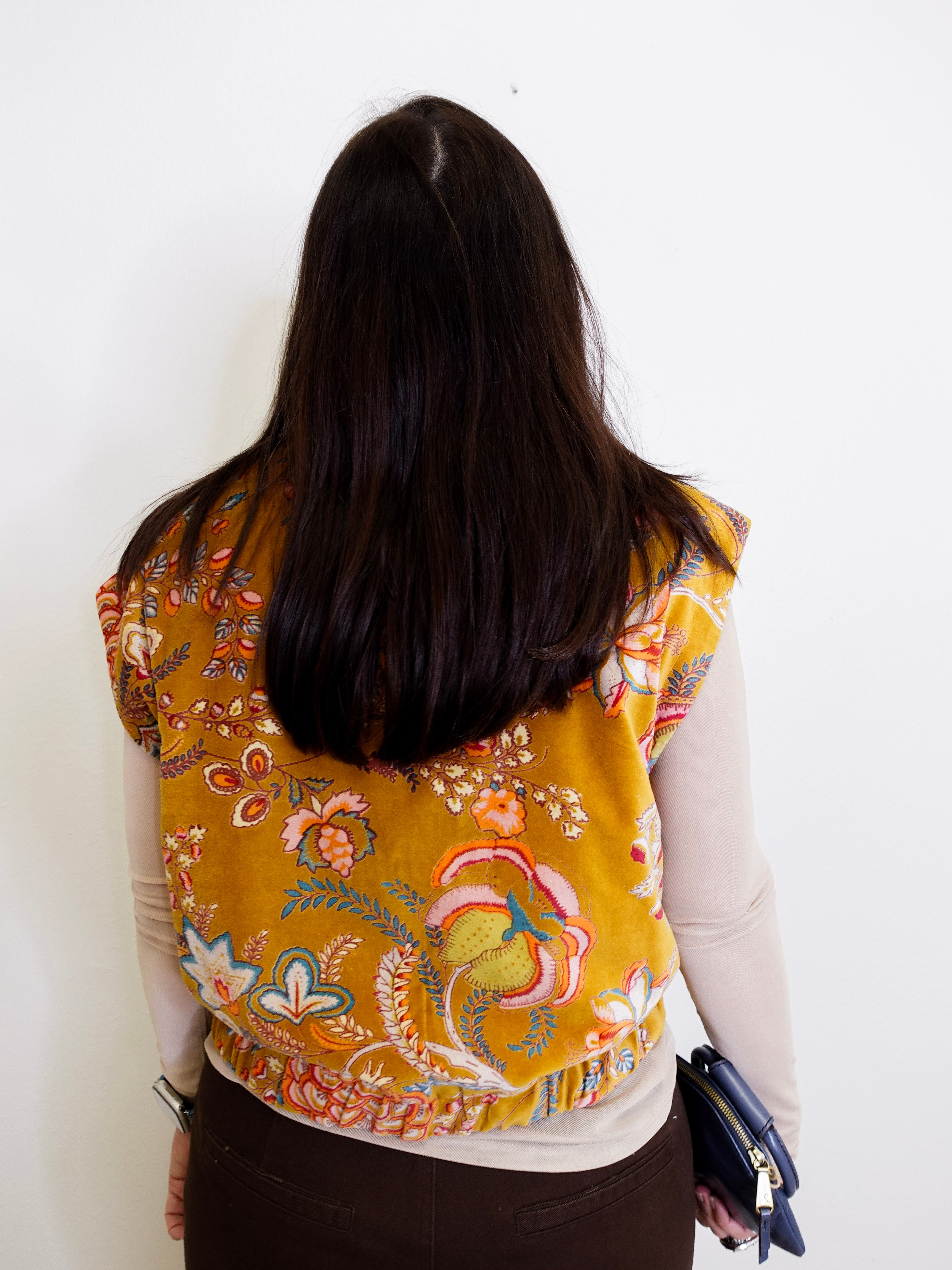 Person wearing a yellow floral vest against a white background