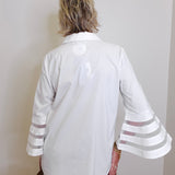 Person wearing a white blouse with sheer sleeves against a plain wall
