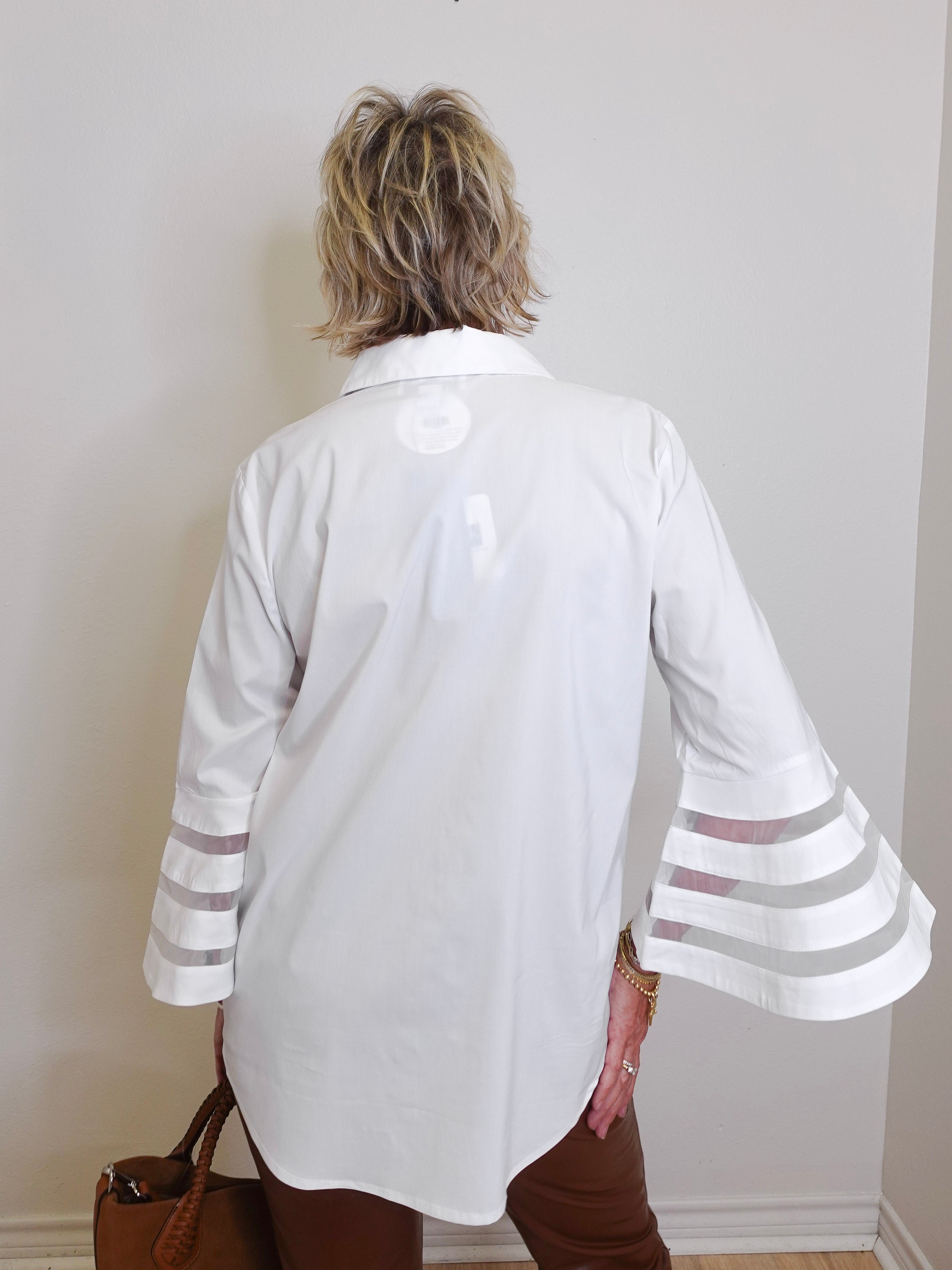 Person wearing a white blouse with sheer sleeves against a plain wall