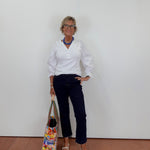 Woman in white shirt and navy pants holding a colorful bag against a plain background