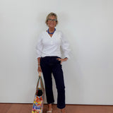 Woman in white shirt and navy pants holding a colorful bag against a plain background