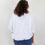 Person wearing a white blouse and blue jeans holding a colorful bag on a plain background