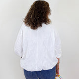 Person wearing a white blouse and blue jeans holding a colorful bag on a plain background