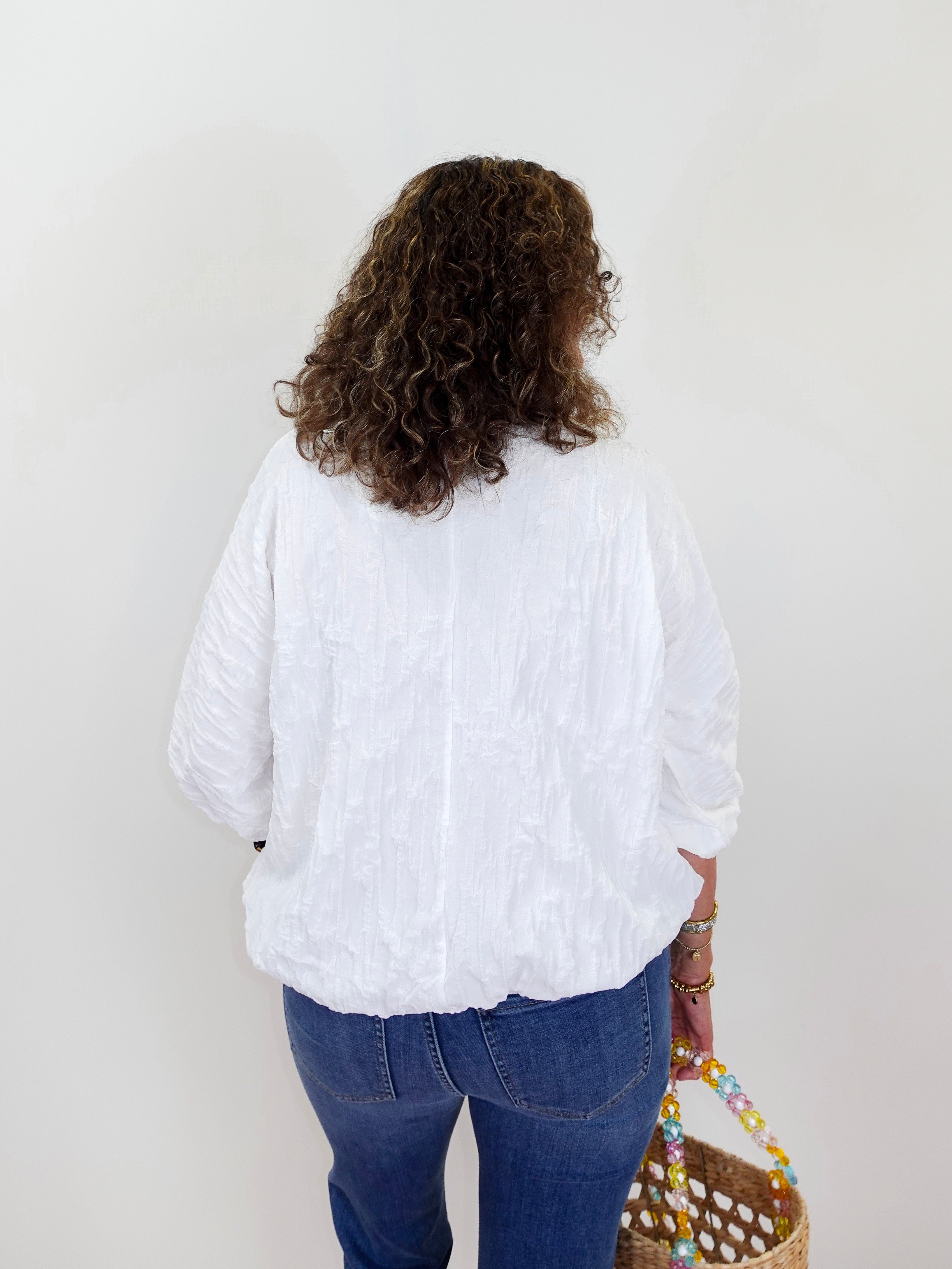 Person wearing a white blouse and blue jeans holding a colorful bag on a plain background