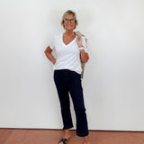 Woman wearing a white shirt and dark pants standing against a plain white wall.