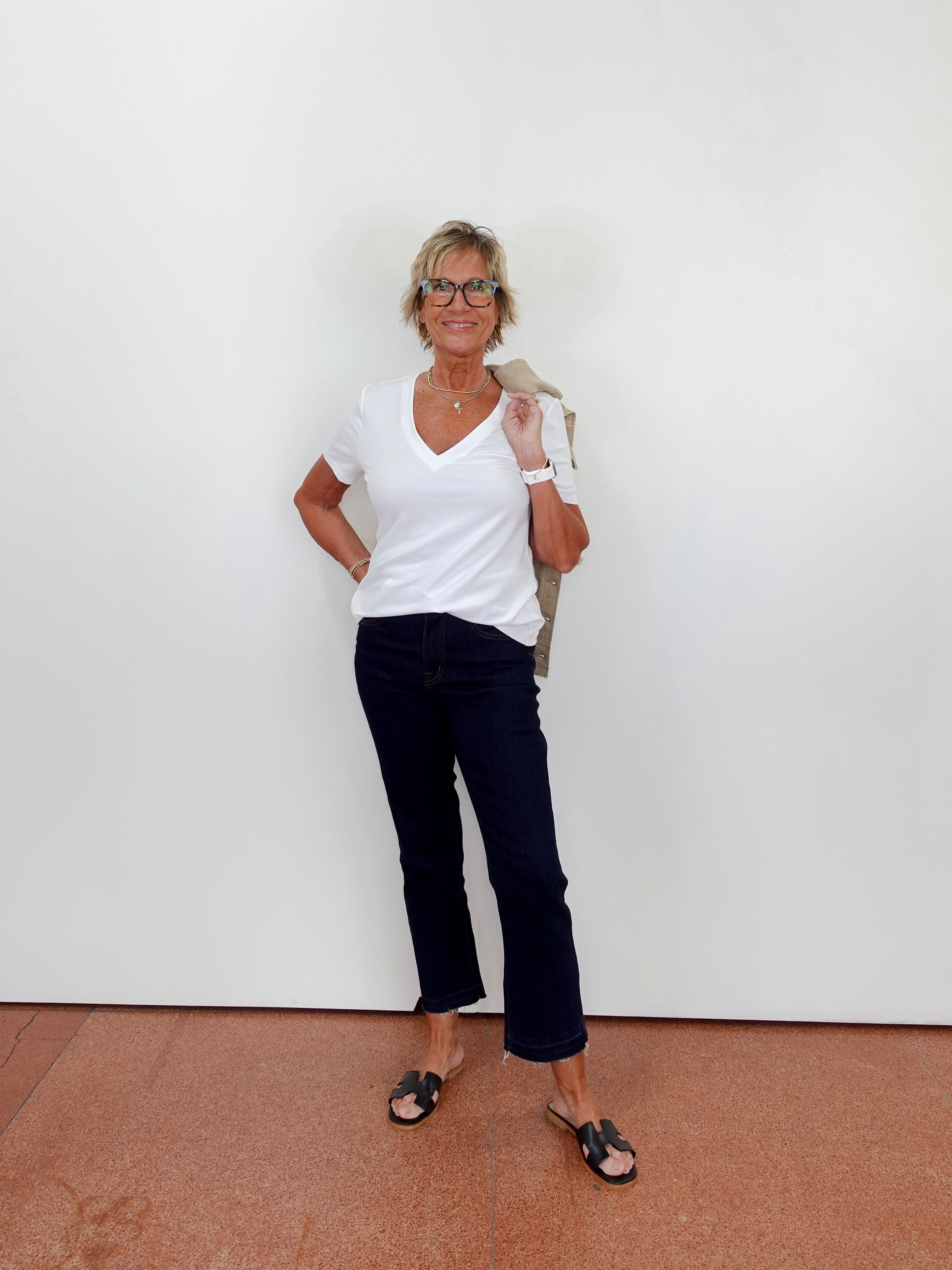 Woman wearing a white shirt and dark pants standing against a plain white wall.