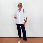 Woman wearing a white shirt and dark pants against a white wall.