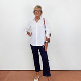 Woman wearing a white shirt and dark pants against a white wall.