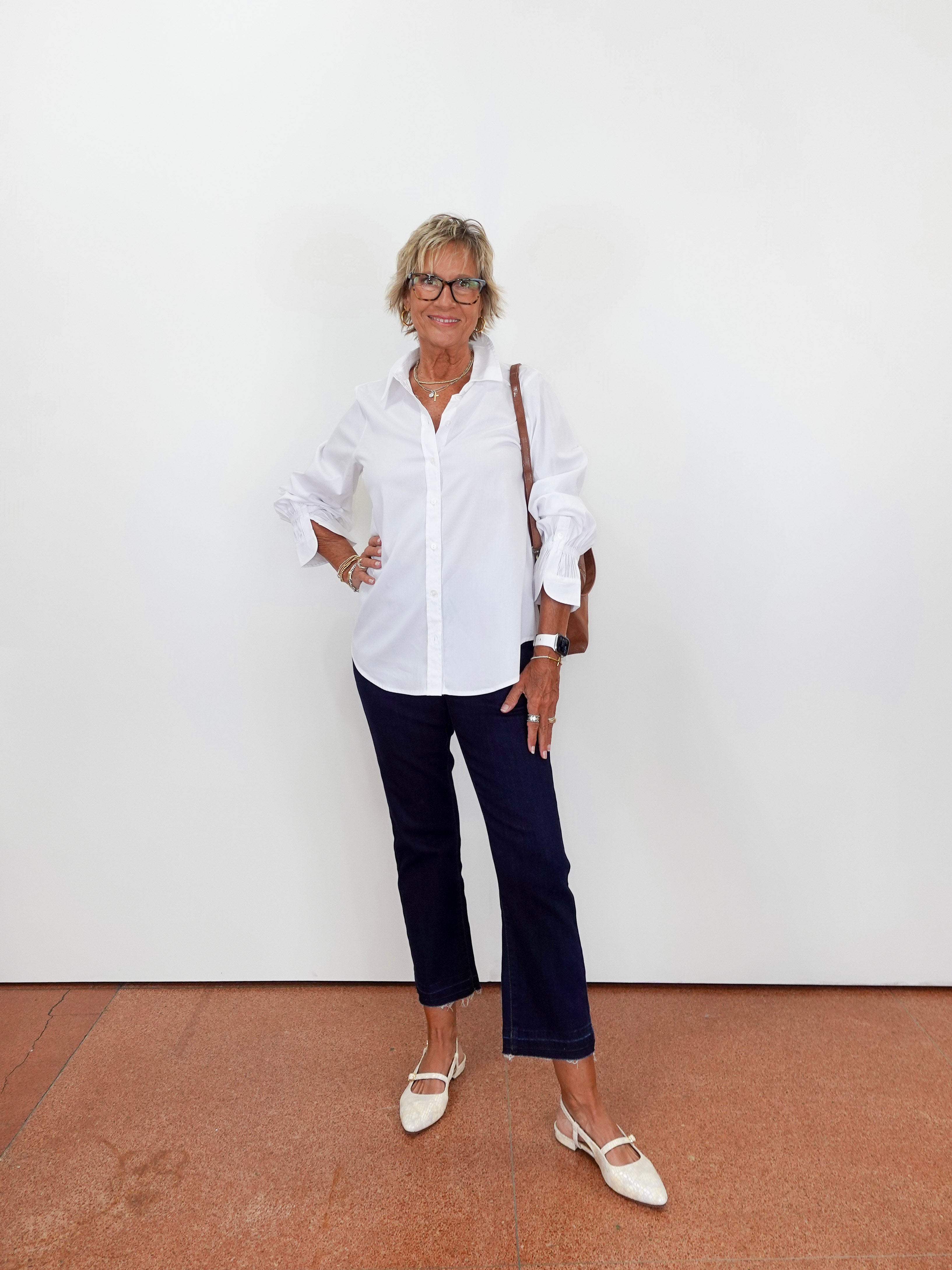 Woman wearing a white shirt and dark pants against a white wall.