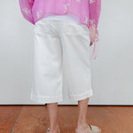 Person wearing a pink floral blouse and white pants on a plain background