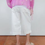 Person wearing a pink floral blouse and white pants on a plain background