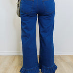 Person wearing blue jeans with ruffled bottom hem on a plain background