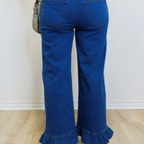 Person wearing blue jeans with ruffled bottom hem on a plain background