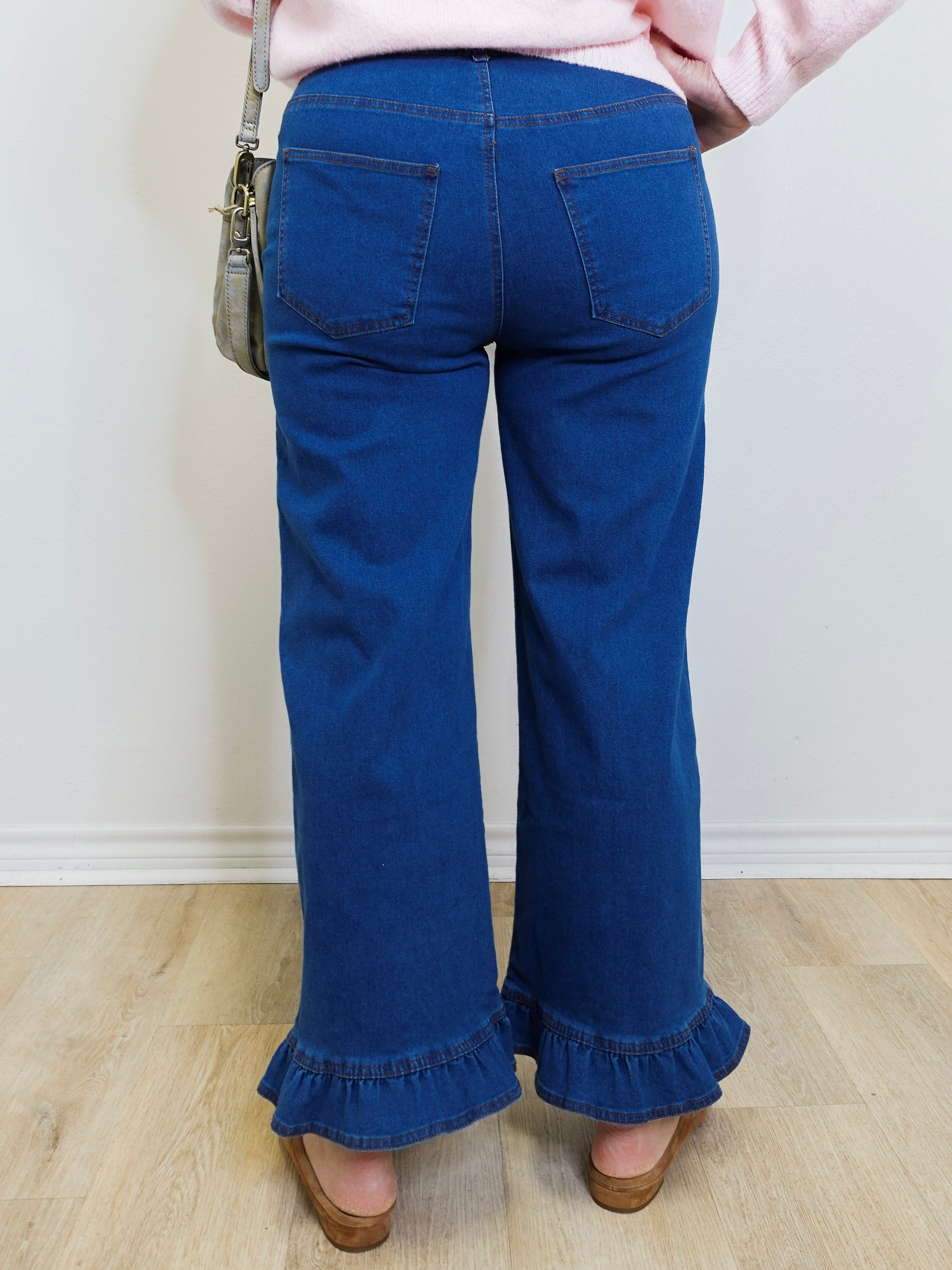 Person wearing blue jeans with ruffled bottom hem on a plain background