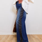 Person wearing blue jeans with a leopard print side panel, standing against a white wall.