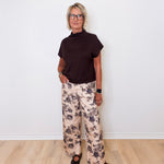 Person wearing a black top and floral pants standing against a white wall.