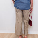 Person wearing a blue shirt and beige pants holding a red handbag against a white wall.