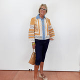 Woman wearing a patterned cardigan over a shirt with dark pants, standing against a white wall.