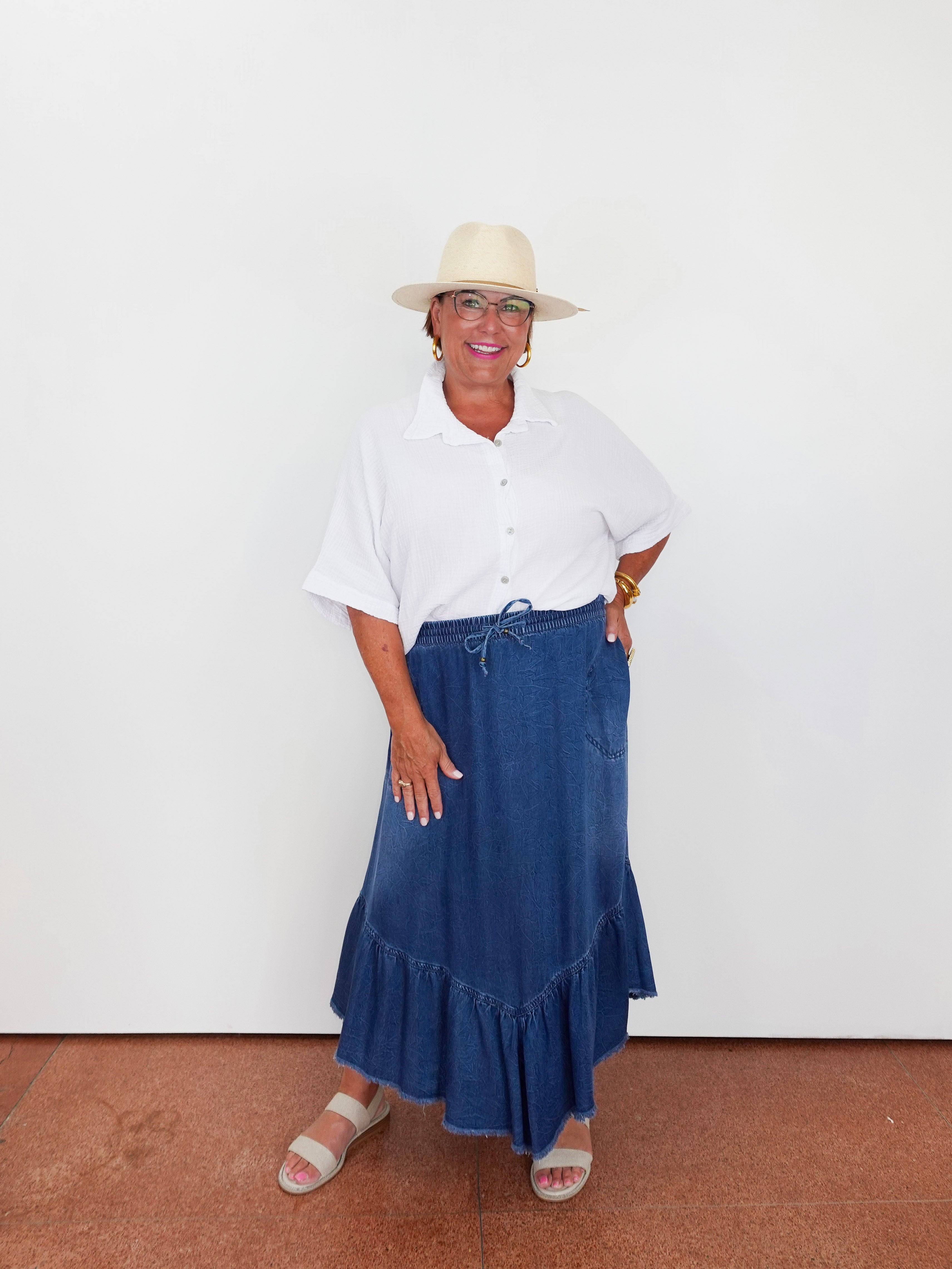 Woman wearing a white shirt, blue denim skirt, and beige hat against a white background