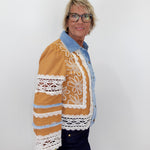 Person wearing a brown jacket with white lace details on a plain background
