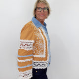 Person wearing a brown jacket with white lace details on a plain background