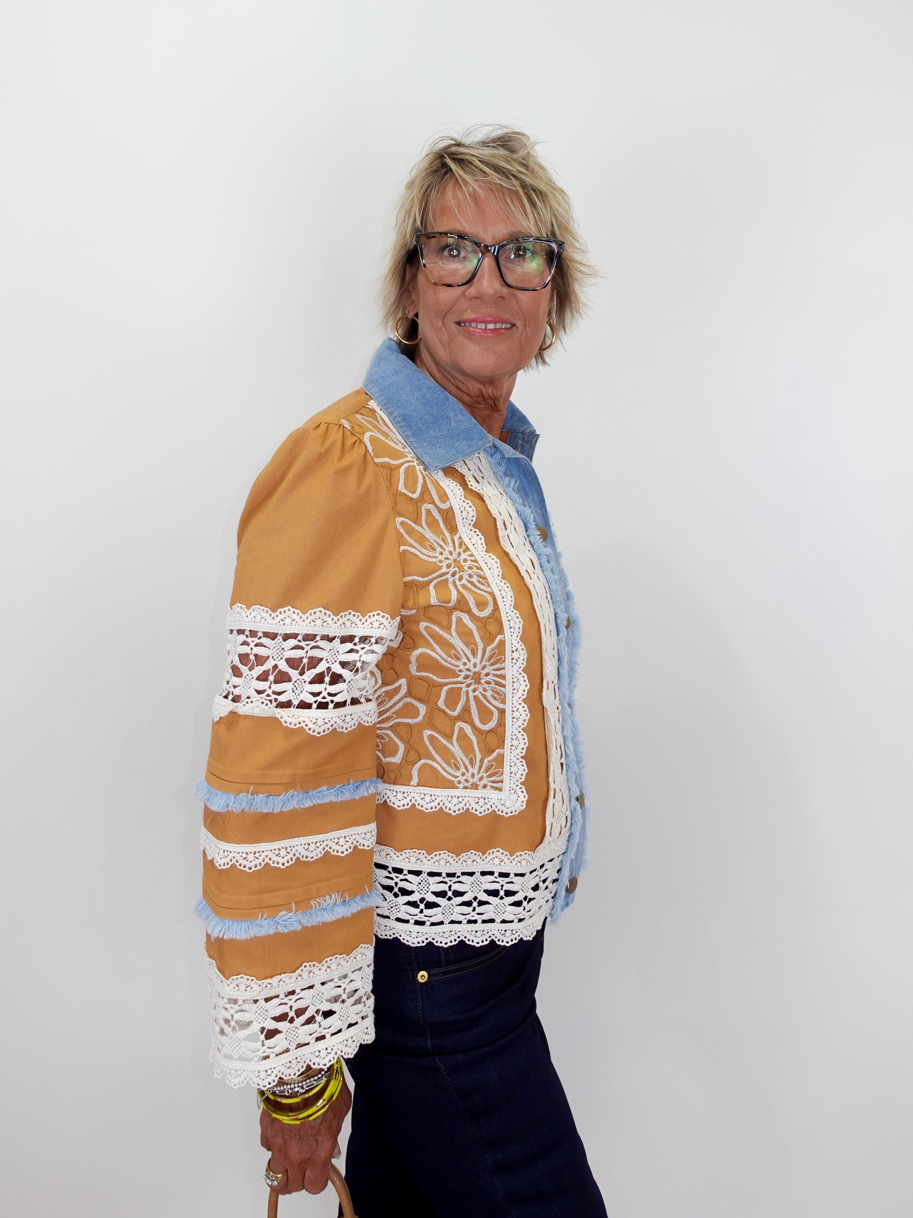 Person wearing a brown jacket with white lace details on a plain background