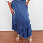 Person wearing a blue denim skirt with a white top on a white background