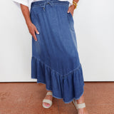 Person wearing a blue denim skirt with a white top on a white background