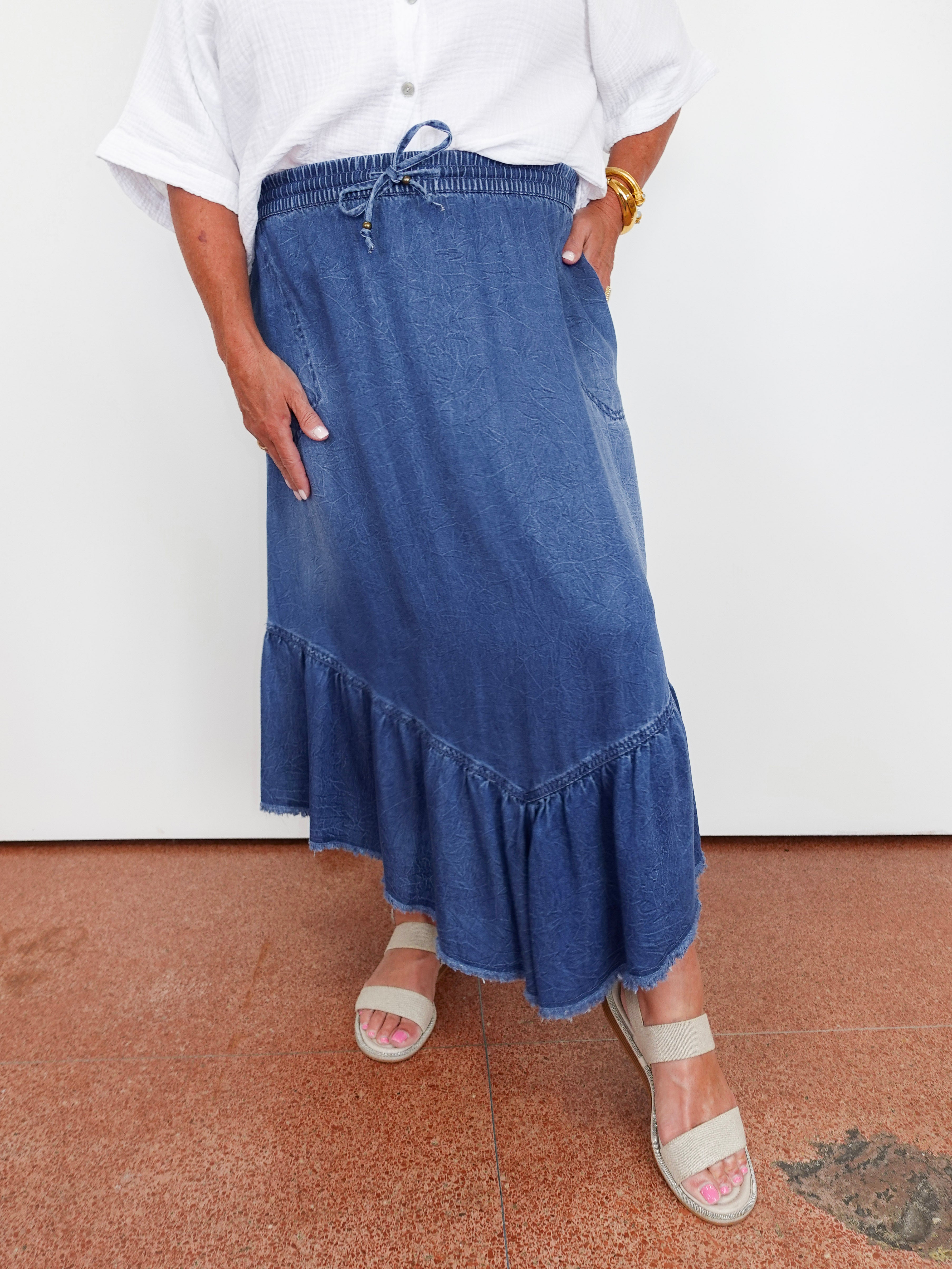 Person wearing a blue denim skirt with a white top on a white background