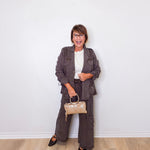Woman in a gray suit holding a beige handbag against a white wall