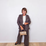 Woman in a gray suit holding a beige handbag against a white wall