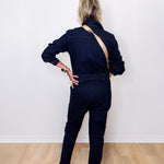 Person wearing a dark denim jumpsuit standing against a white wall.