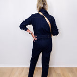 Person wearing a dark denim jumpsuit standing against a white wall.