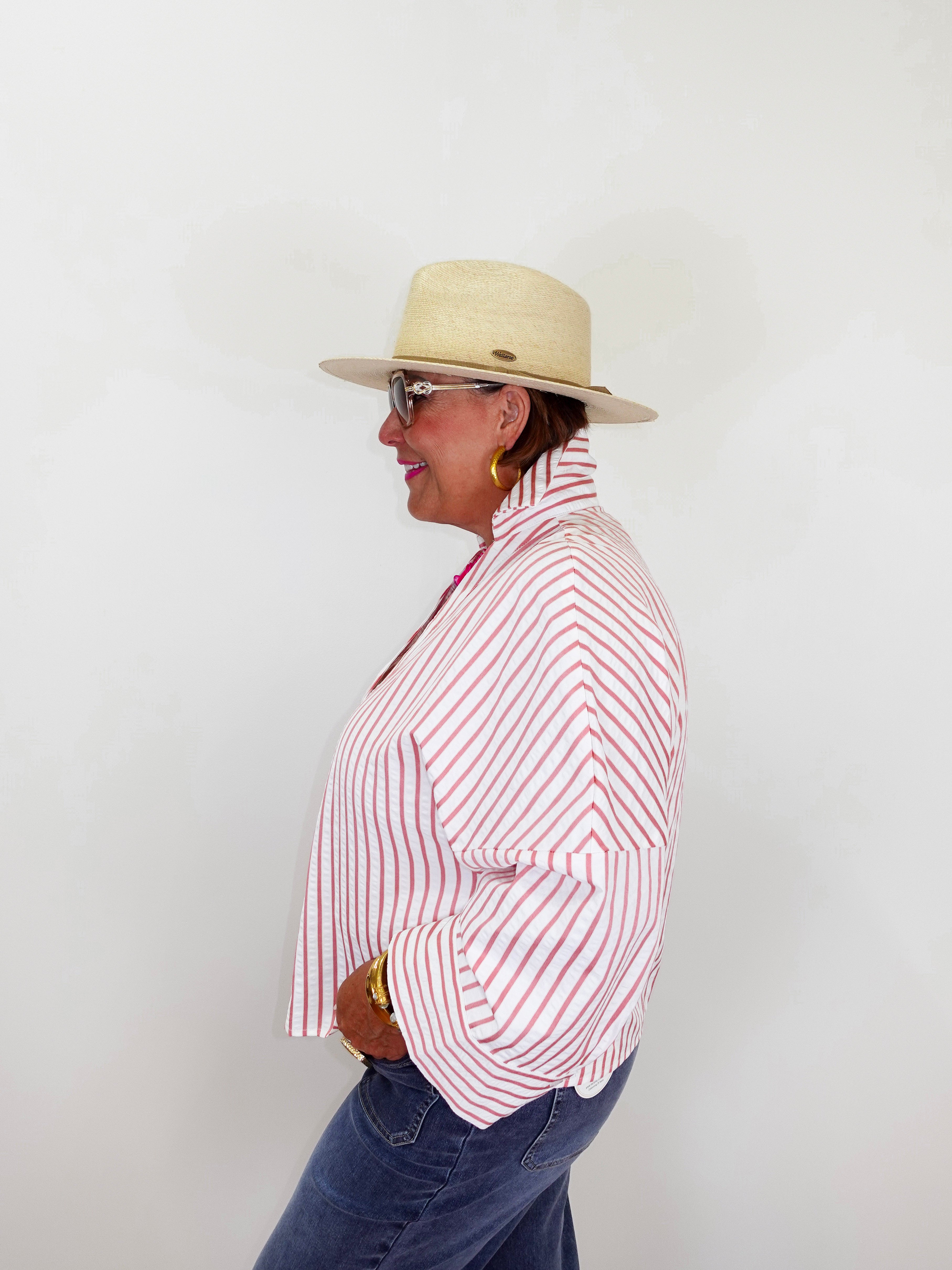 Person wearing a red and white striped shirt, blue jeans, and a beige hat against a white background
