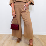Person wearing a beige outfit with wide-leg pants and holding a maroon handbag.