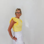 Woman wearing a yellow top with lace details and a white skirt against a plain background