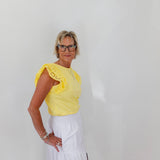 Woman wearing a yellow top with lace details and a white skirt against a plain background