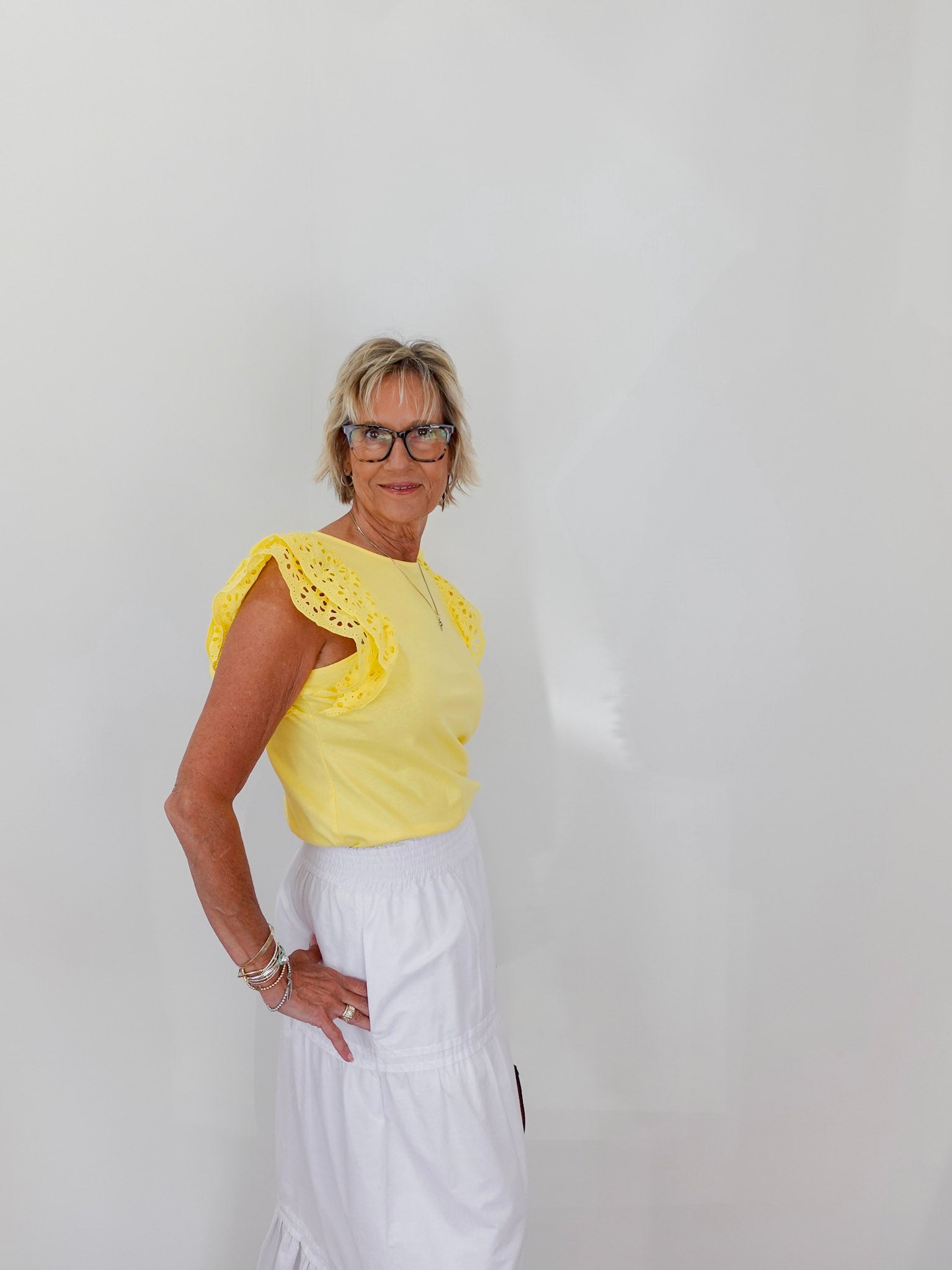 Woman wearing a yellow top with lace details and a white skirt against a plain background