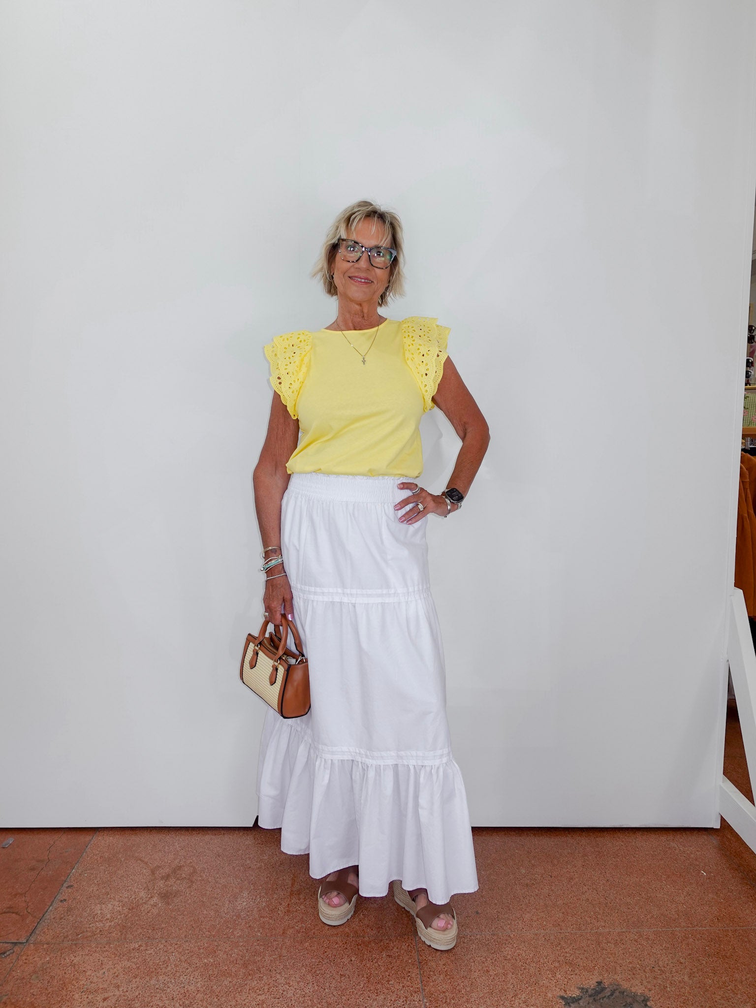 Woman wearing a yellow top and white skirt against a white wall.