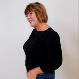 Woman wearing a black top and blue jeans against a white background