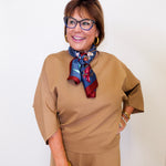Woman wearing a beige outfit with a colorful scarf against a white background