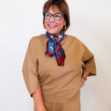 Woman wearing a beige outfit with a colorful scarf against a white background