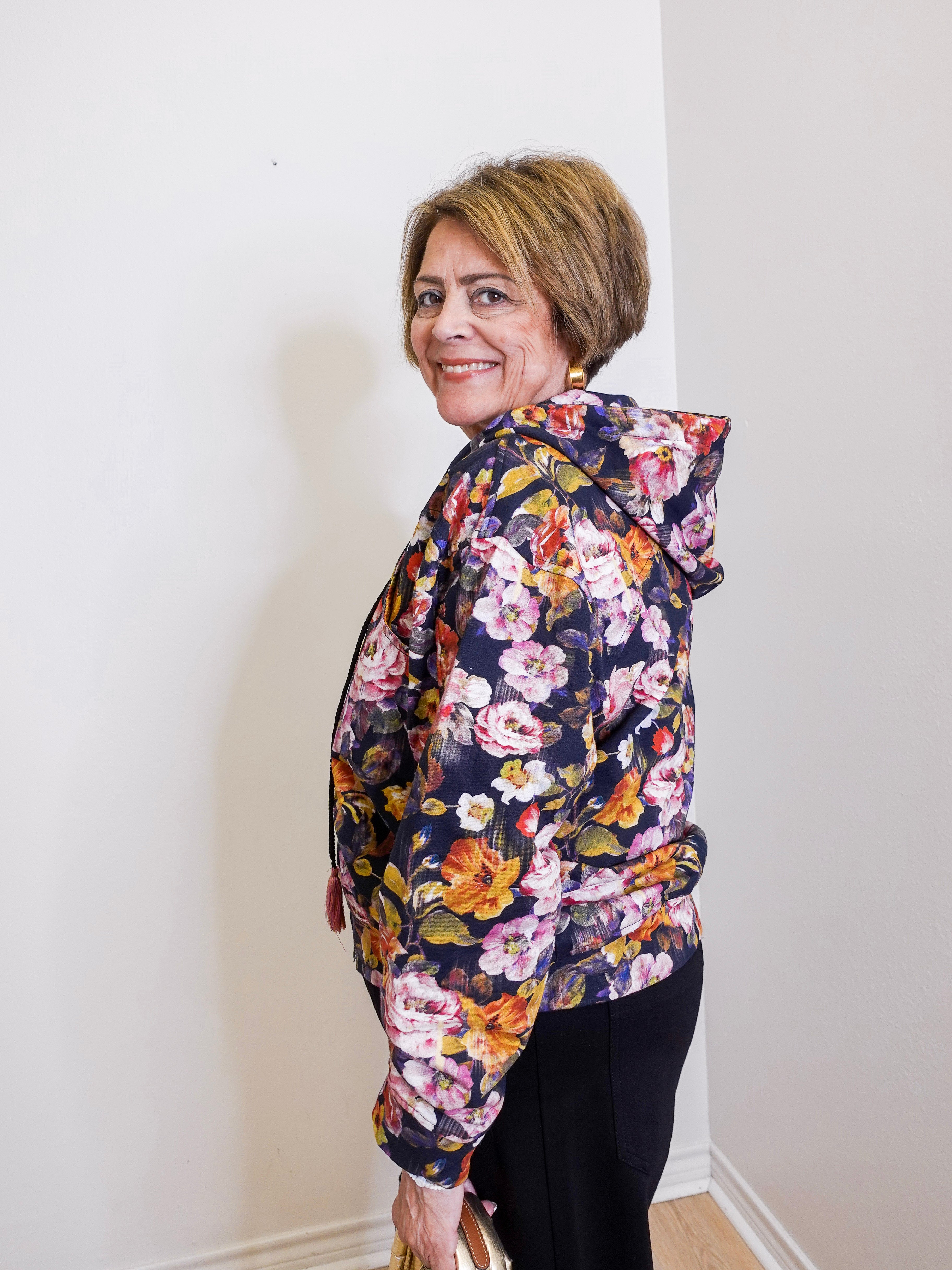 Woman wearing a floral print hooded zip front jacket from Apny in front. white background. 