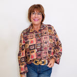 Woman wearing a patterned blouse and jeans against a white background