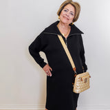 Woman in a black dress with a gold handbag against a white wall