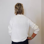 Person wearing a white ribbed sweater against a plain background